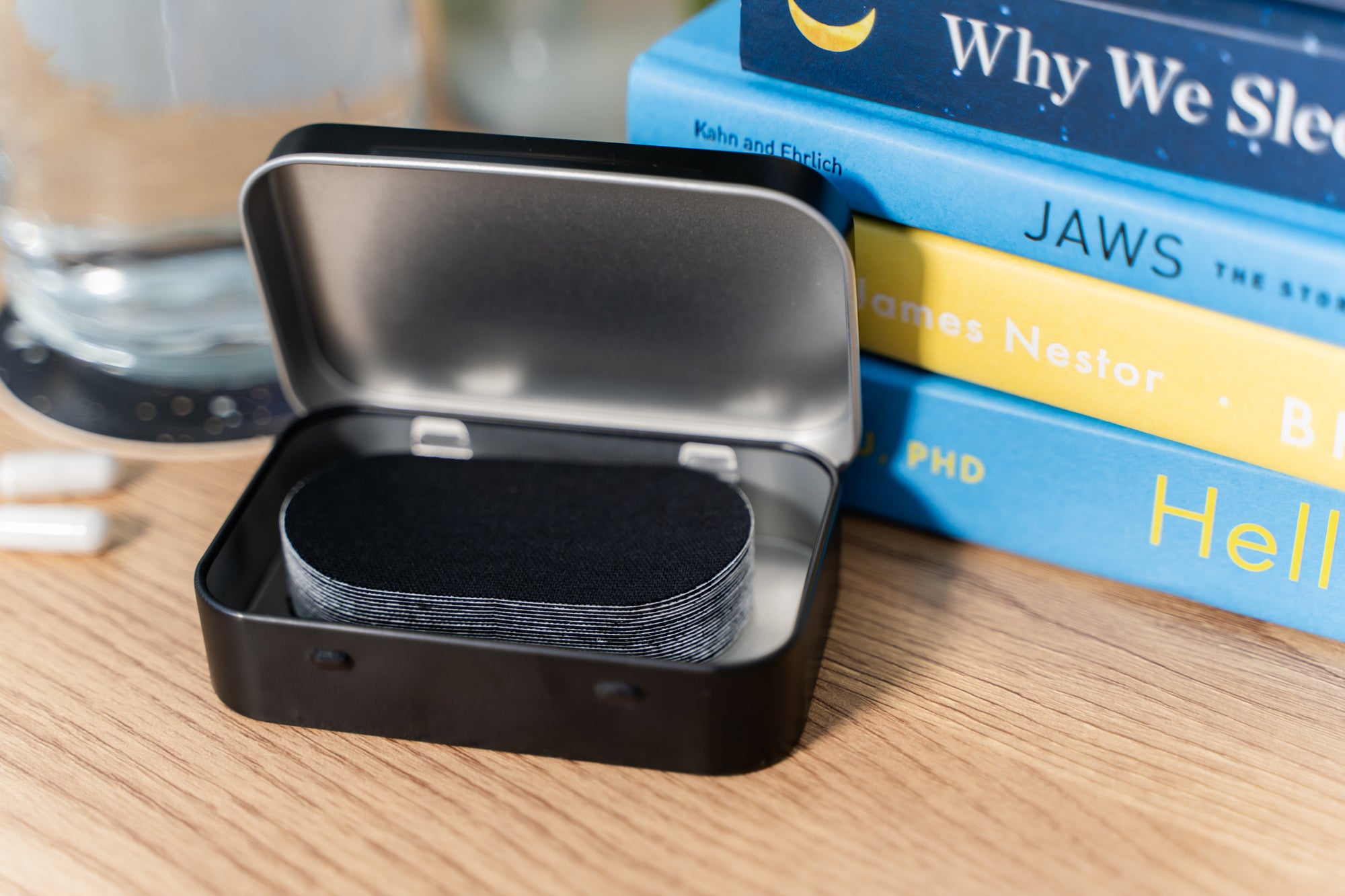 Stack of Books with a Knocked Mouth Tape Tin, Open, showing the mouth tape inside.