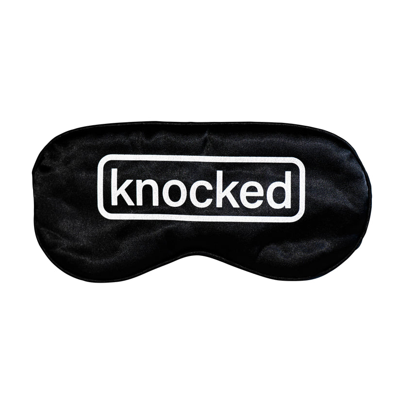 Black sleep mask with the word 'knocked' printed in white.
