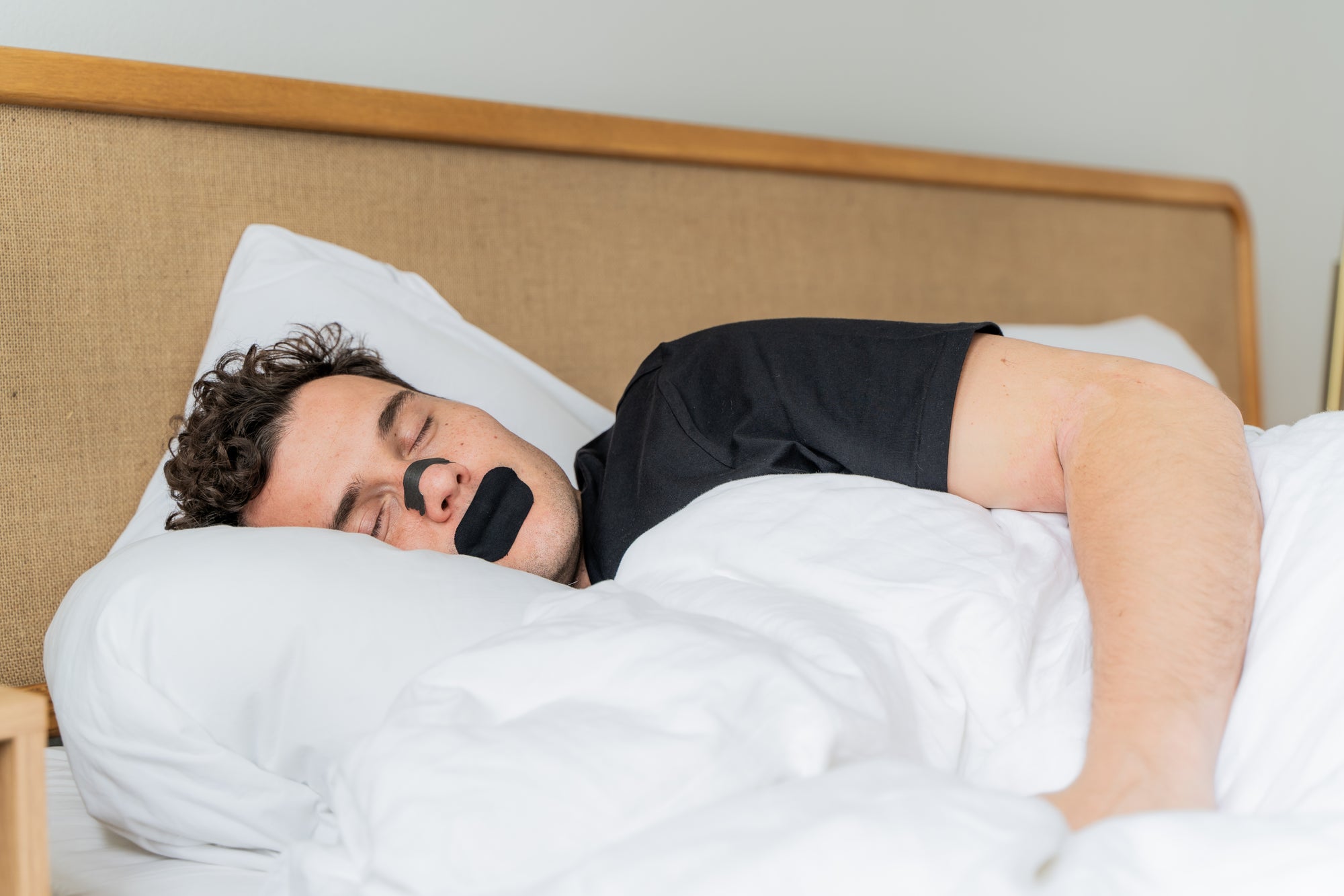 Man sleeping in bed with Knocked Nose Strips and Mouth Tape