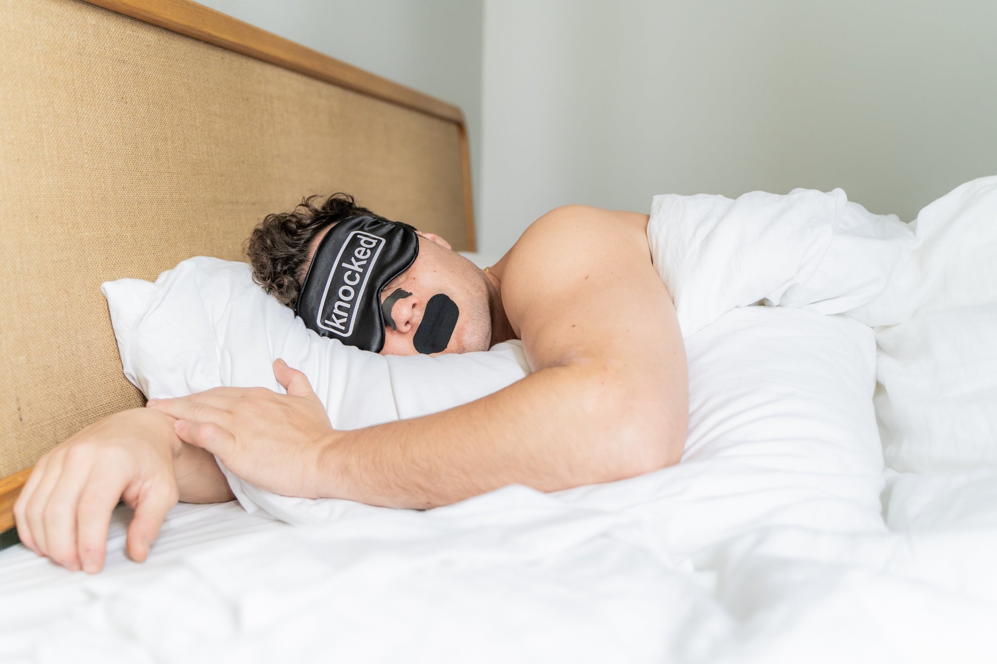 man sleeping in bed with knocked sleep stack, eye mask, nose strips, and mouth tape
