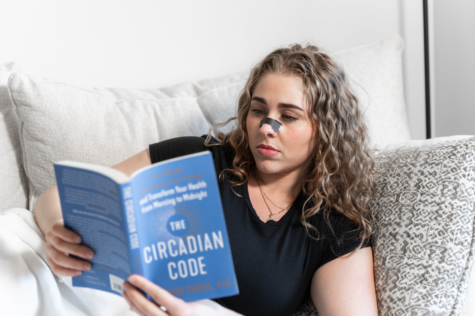 Woman reading the circadian code while on the couch using Knocked Nose Strips