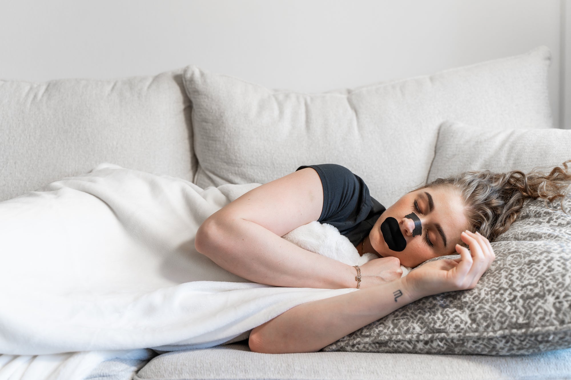 Woman sleeping on couch with Knocked nose strips and knocked mouth tape 