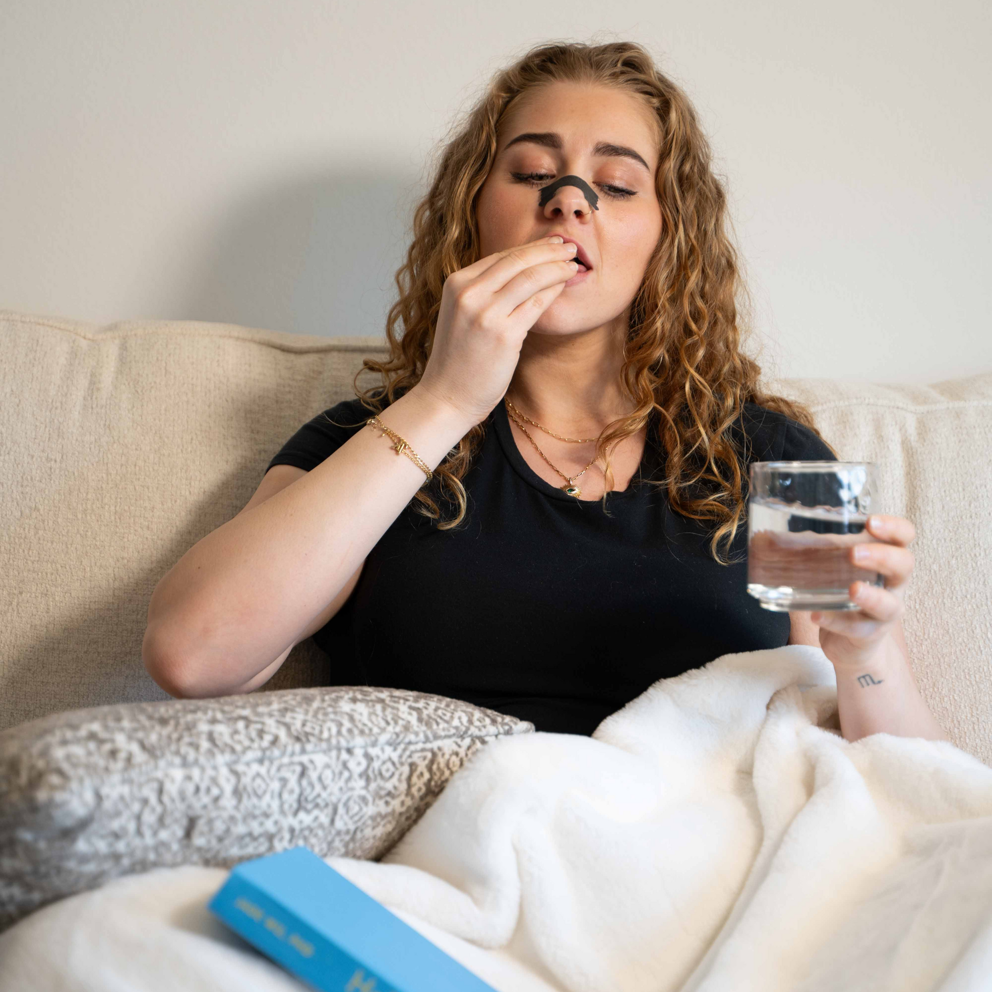 Taking Knocked Sleep Support on the couch with a glass of water, cozy blanket, and Hello, Sleep Book